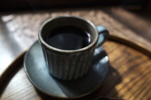陶器のカップに注がれたコーヒー。落ち着いた雰囲気の中で一息つける温かみのある風景。