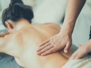 男性セラピストが女性の背中に優しく触れ、温かい手のぬくもりで心身をゆるめている様子。撫でるようなノンオイルマッサージの施術シーン。