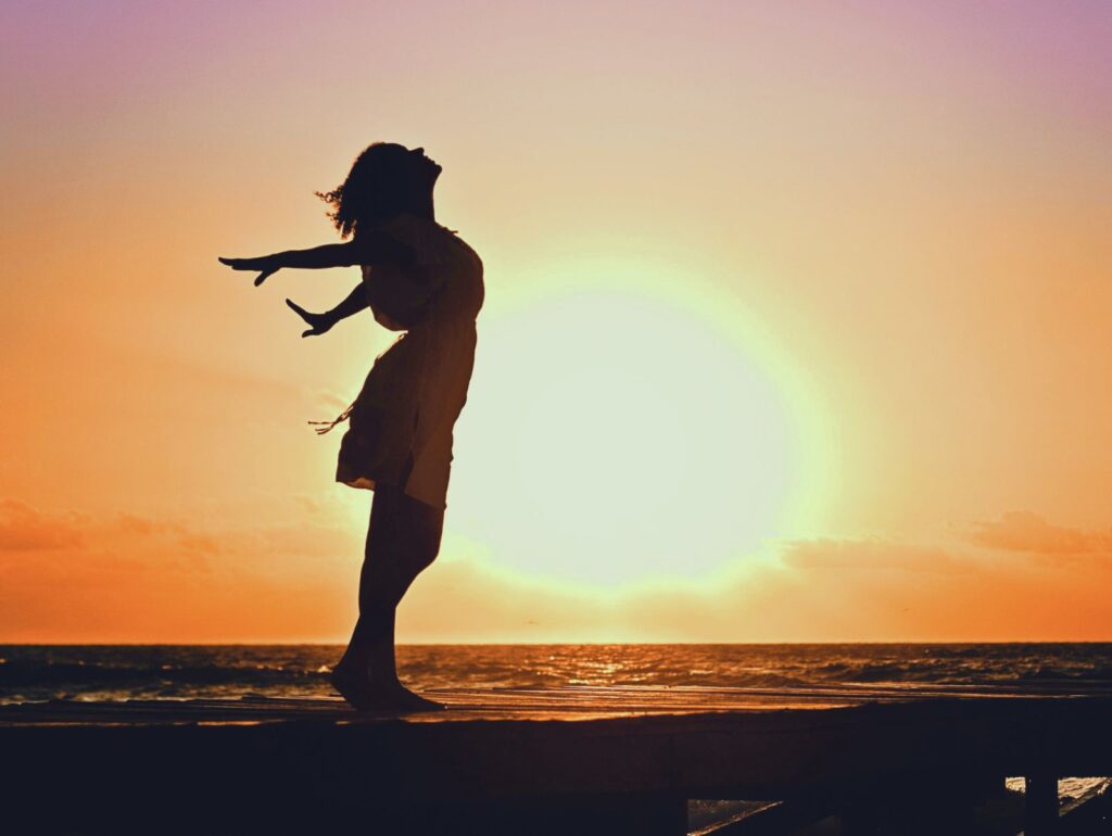 夕陽の中で自由に腕を広げる女性。自分軸を取り戻し、心からの解放と安心を感じている姿。