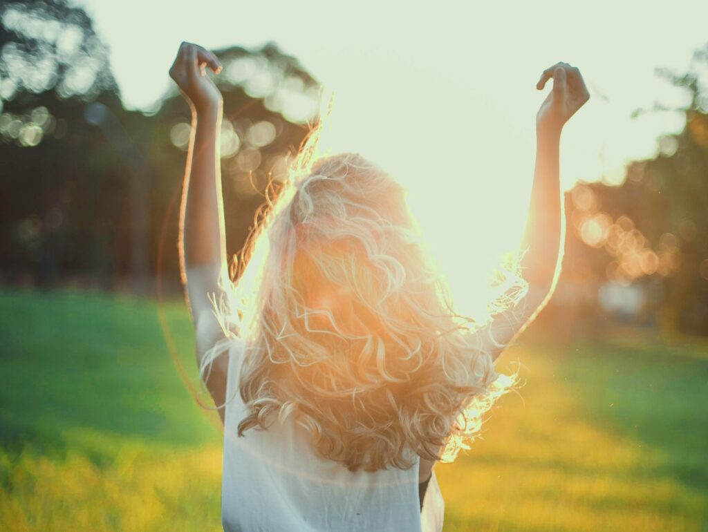 朝日を浴びて両手を広げる女性。光に包まれながら、自分らしさと自由を取り戻す瞬間。