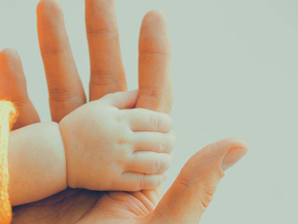 大人の手のひらに、赤ちゃんの小さな手が重なっている。
ぬくもりと安心感を感じさせる優しい瞬間の写真。