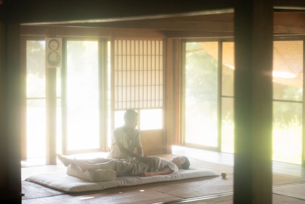 伝統的な和室で行われる睡眠マッサージ(自然体施術)の様子。施術者が穏やかに手を添え、受け手が深くリラックスして横たわっている。柔らかな光が差し込み、静けさと安心感が漂う空間。