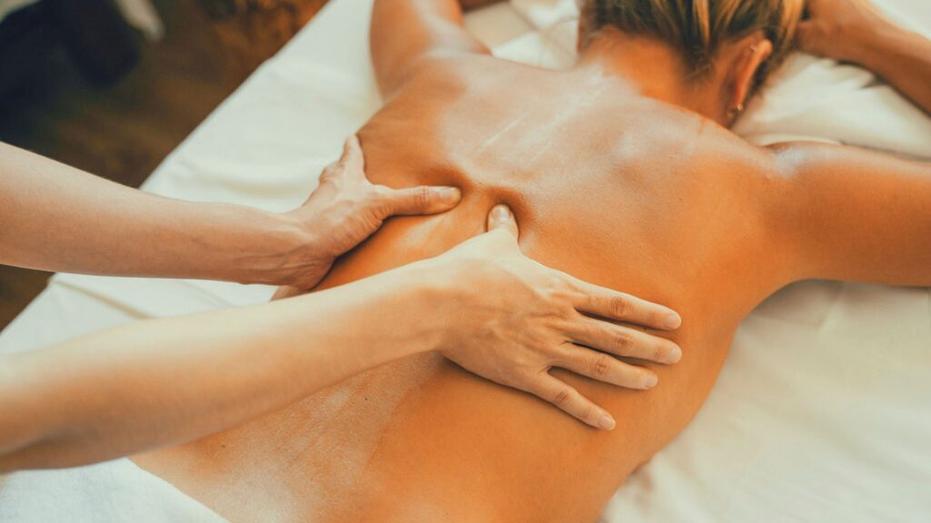 「男性セラピストが日本人女性に背中のリンパマッサージ（リンパドレナージュ）を行っている様子。優しい手技でリンパを流し、むくみや緊張をケアする施術シーン。」