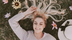 芝生の上で目を閉じて微笑む女性。冷えや肩こり、腰痛から解放され、心と身体がゆるんでいる様子を表すリラックスイメージ。