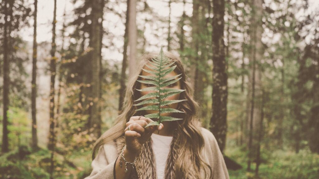 森の中で自然とつながる女性の姿。女性性とは何かを象徴するように、やさしく葉を手にする女性。