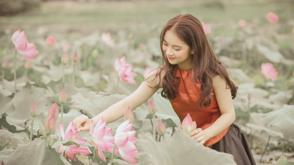 女性性を高めるために自然と触れ合い、蓮の花に手を伸ばして優しく触れている女性の写真｜女性性高める方法