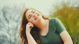 自然の中で目を閉じて微笑む女性。心と身体がゆるみ、三大欲求（睡眠・食欲・性欲）が満たされることで感じる幸せと安心感を表現したイメージ