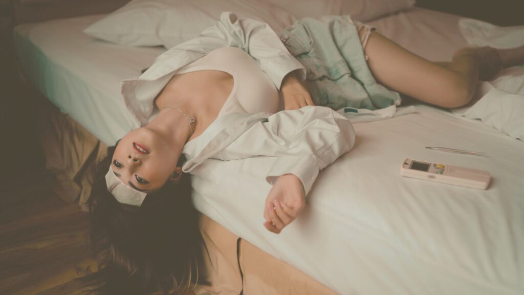ベッドの上で力を抜いて横たわる女性。心と身体が限界まで頑張り、病気や不調が愛の信号として現れる瞬間を象徴するイメージ。ストレスや緊張、心身の疲労と向き合い、休息と回復の大切さを伝えている。