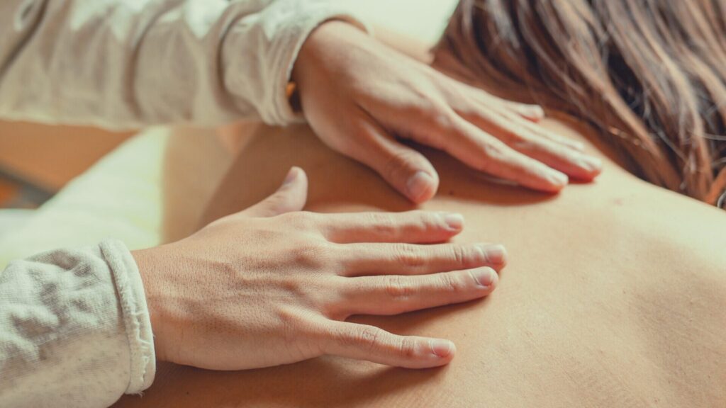 素手で背中に優しく触れ、撫でるようにリンパを促すノンオイルリンパドレナージュの施術風景