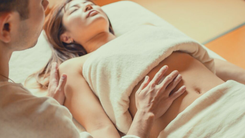 チネイザン(腸もみ)施術中の様子。ベッドに横たわる女性のお腹に、セラピストがやさしく手を添え、腹部を緩めながら自律神経と内臓の緊張を整えている場面。