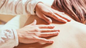 女性の背中にやさしく触れることで安心感を引き出す施術シーン。女性性や感覚を取り戻すためのリラクゼーションケア